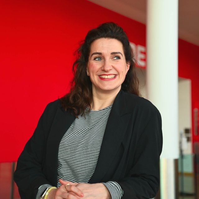 Vrouw met streepjes t-shirt en zwart colbert lacht naar de camera