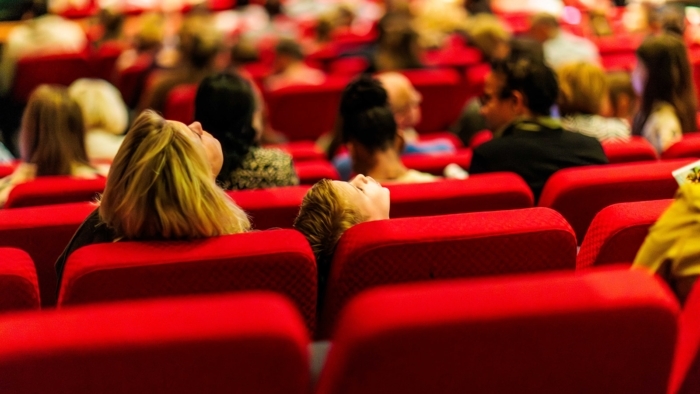 Een indrukwekkend overzicht van de moderne, grote theaterzaal in het Nieuwe Luxor. Je ziet rijen met comfortabele rode stoelen die in een lichte boog naar het podium lopen, met daarboven de verschillende balkons en de professionele theaterverlichting aan het plafond.